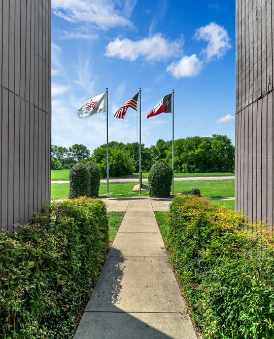 the entrance to a building with flags flying in the background at The Arlington Park Apartments