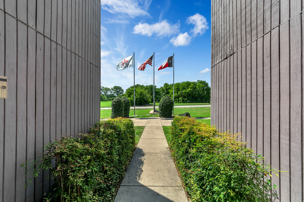 the entrance to a building with flags flying in the background at The Arlington Park Apartments