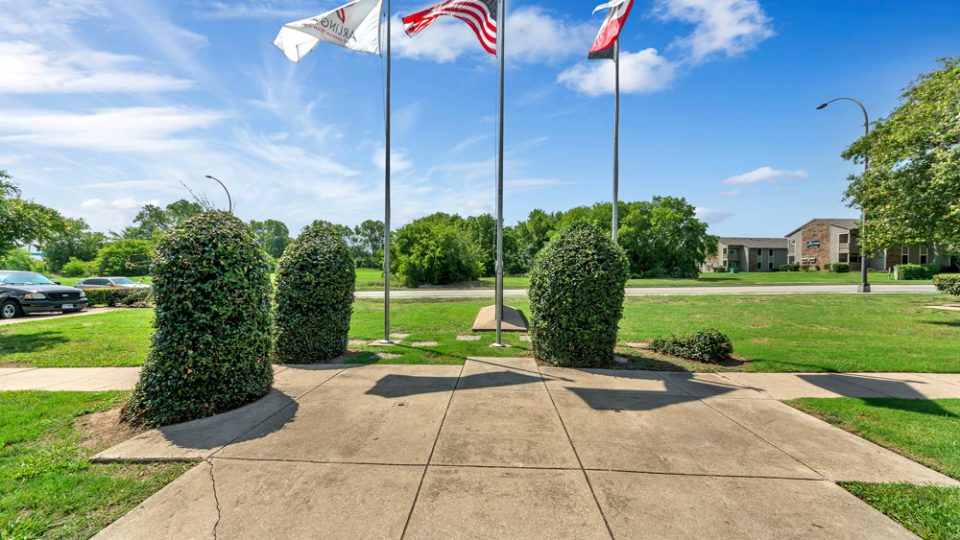 a park with flags and a flag pole in front of it at The Arlington Park Apartments